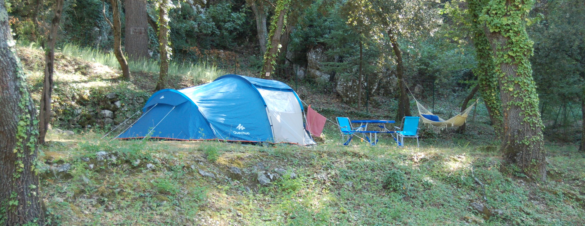 Une grande tente bleue et blanche montée sur un emplacement ombragé du camping les Royères du Prieuré de Maubec