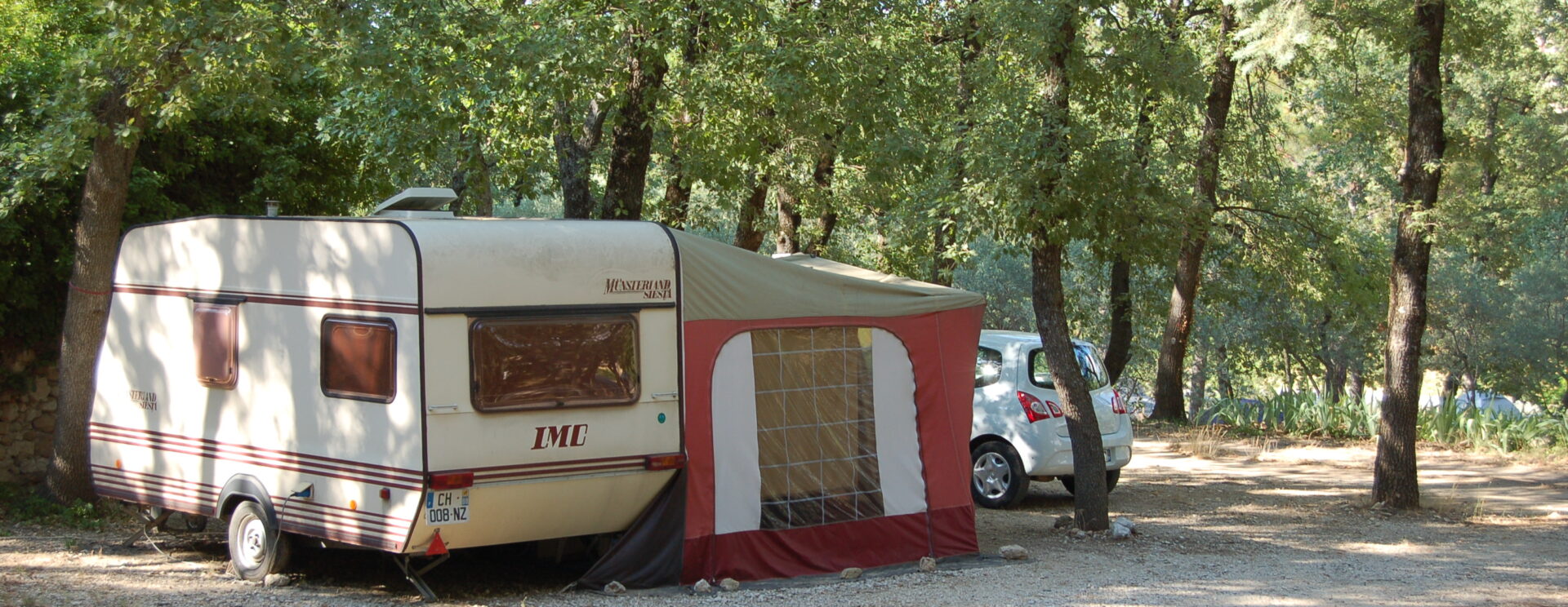 Une caravane et son haut-vent stationnés près d'une voiture sur un emplacement du camping Les Royères du Prieuré de Maubec